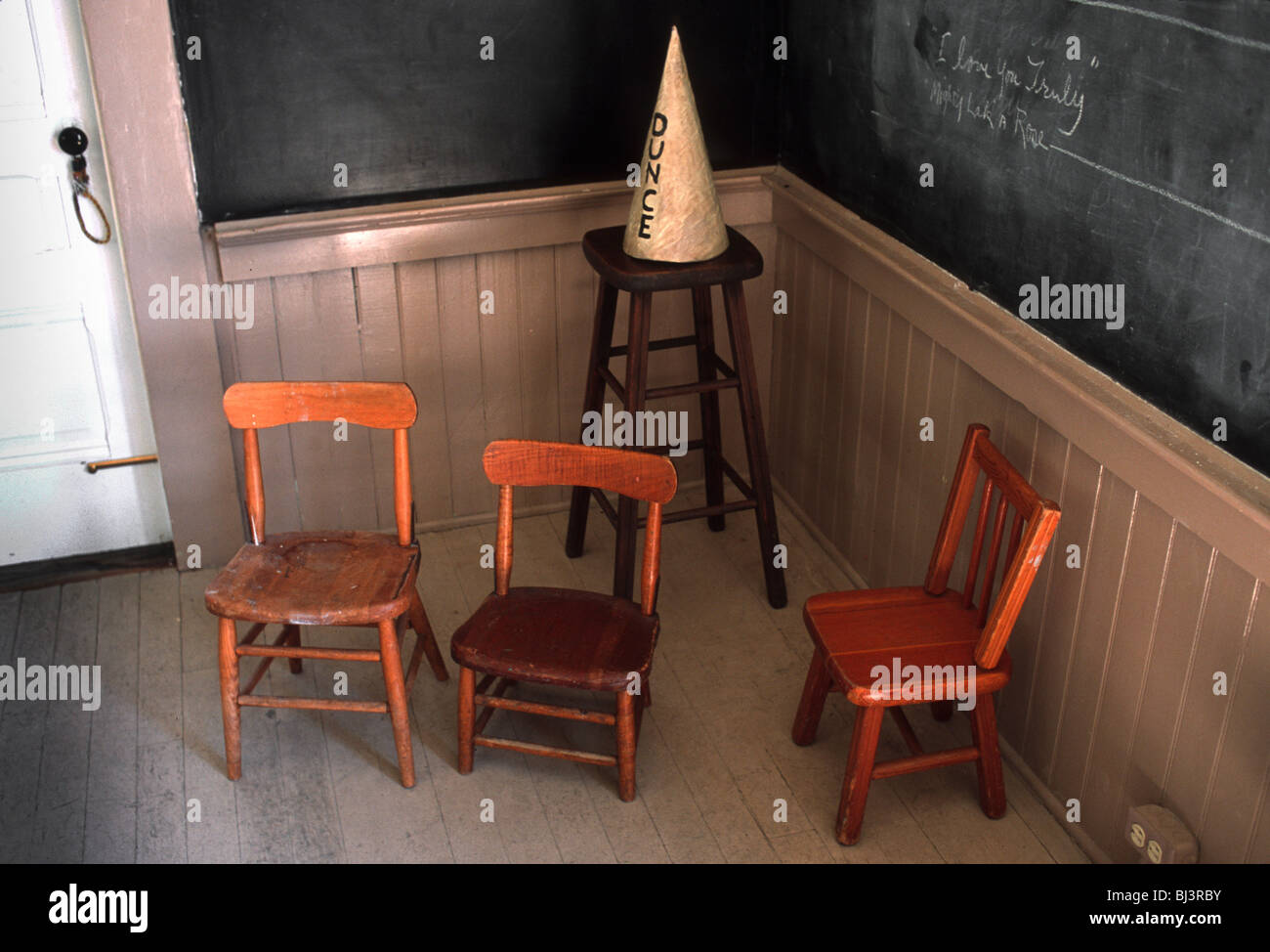 Ein Dunce Cap und Schule Stühle durch eine altmodische Tafel. Stockfoto