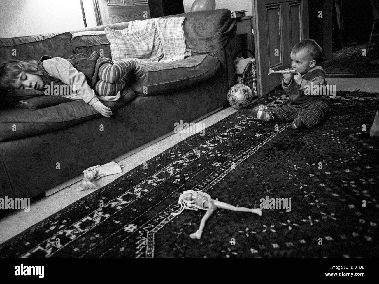 Als ihr Bruder spielt, nimmt ein dreieinhalb Jahre altes Mädchen ein Nickerchen am Nachmittag auf dem Sofa in ihrem Hause Südlondon. Stockfoto