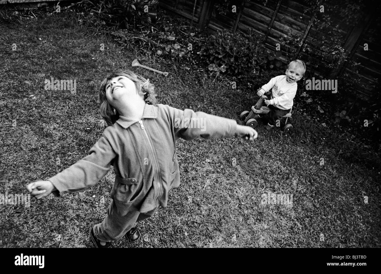 Ein drei Jahre altes Mädchen wirft den Kopf zurück mit Freude beim Spielen mit ihren jungen ein-Jahr-alte Bruder im Garten hinter dem Haus. Stockfoto