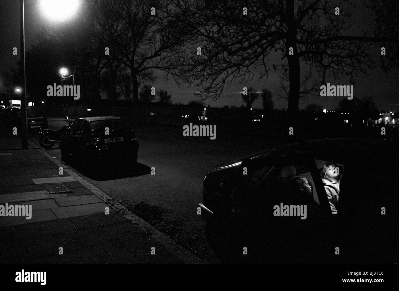 Spät in der Nacht in einer South London Straße bleiben zwei kleine Kinder schnell Einschlafen auf der Rückseite ihrer Eltern Auto. Stockfoto