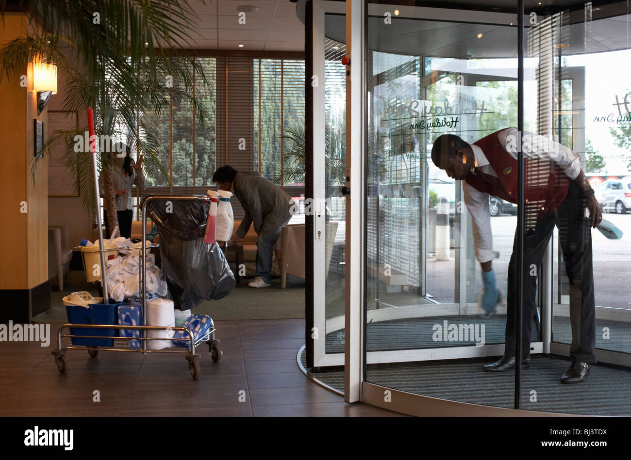 Ein Mann mit schwarzen Ethnizität beugt sich nach vorne um die Glas-Drehtüren am Eingang des Hotels in Paris zu wischen. Stockfoto