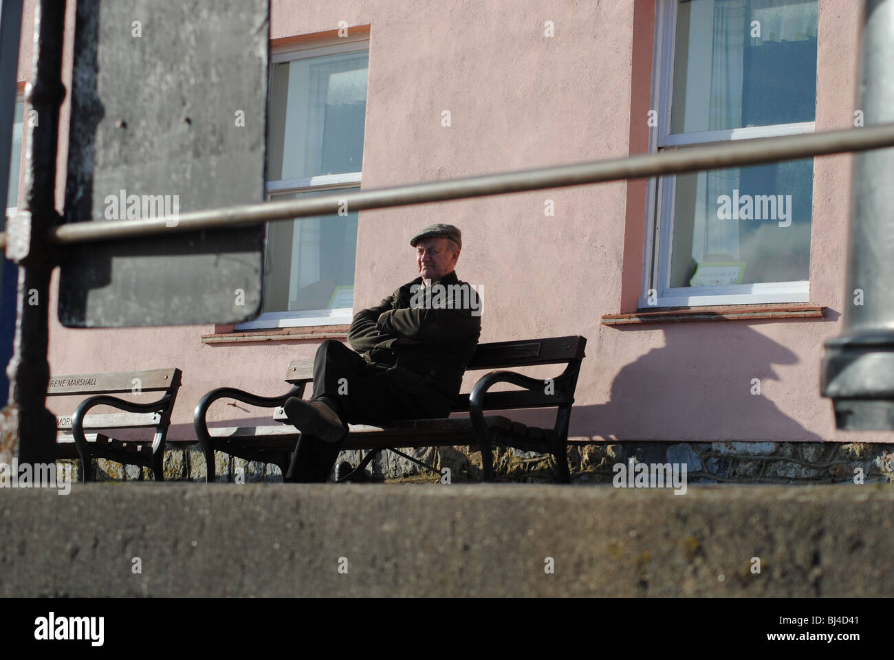 Alter Mann auf Bank vor Rosa Haus. Marine Parade, Lyme Regis, Dorset, England Stockfoto