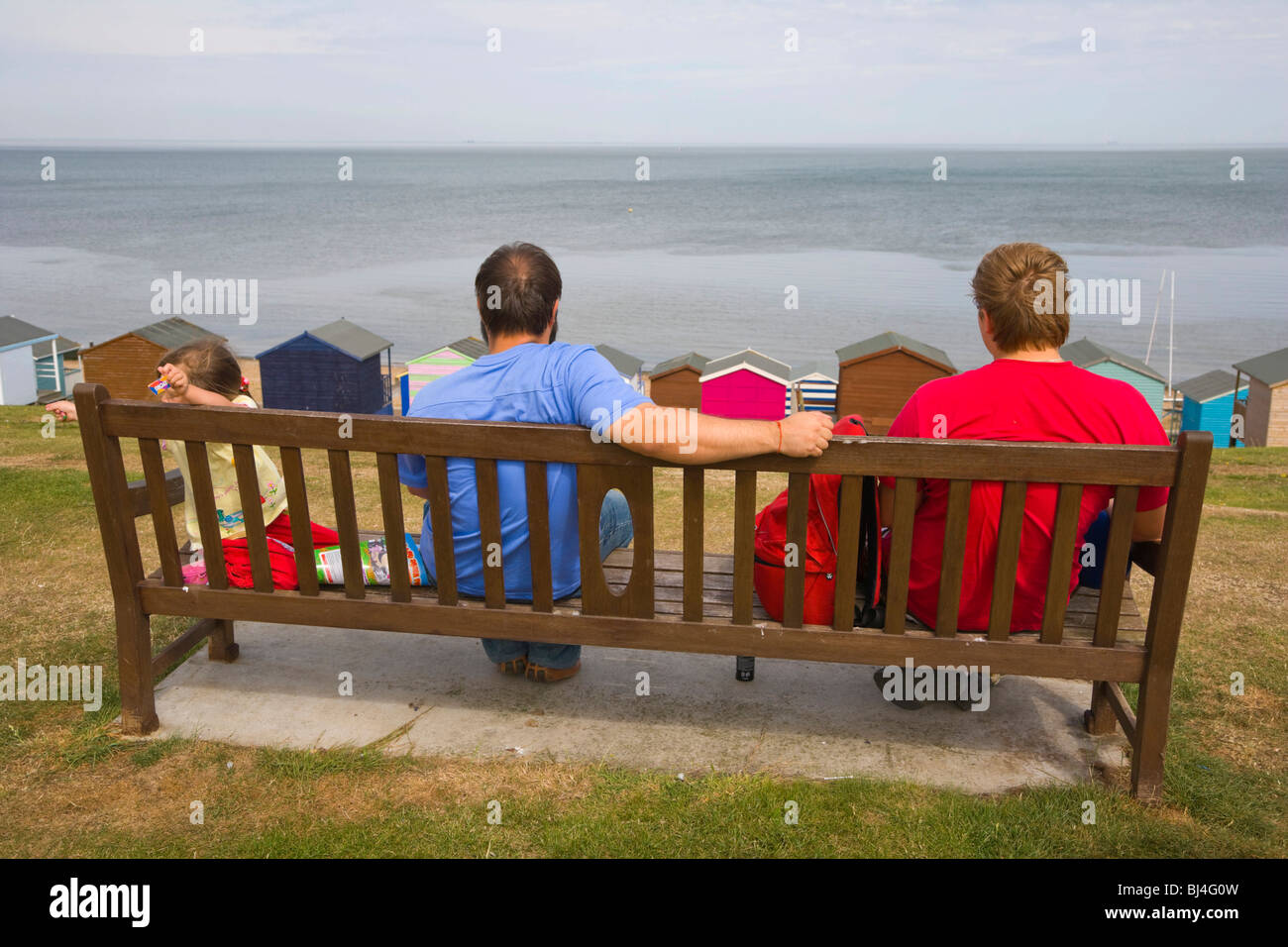 Familie auf einer Bank mit Blick auf Strand, Hütten und Meer bei Tankerton in der Nähe von Whitstable, Kent, England, Vereinigtes Königreich, Europa Stockfoto