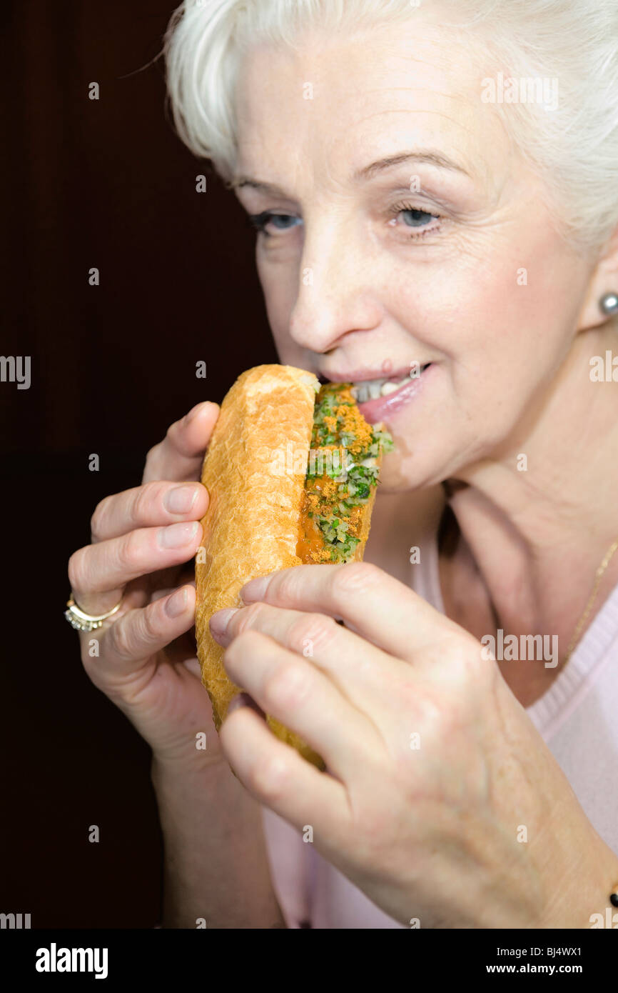 Eine Frau in eine Wurst in einem Baguette zu beißen Stockfoto