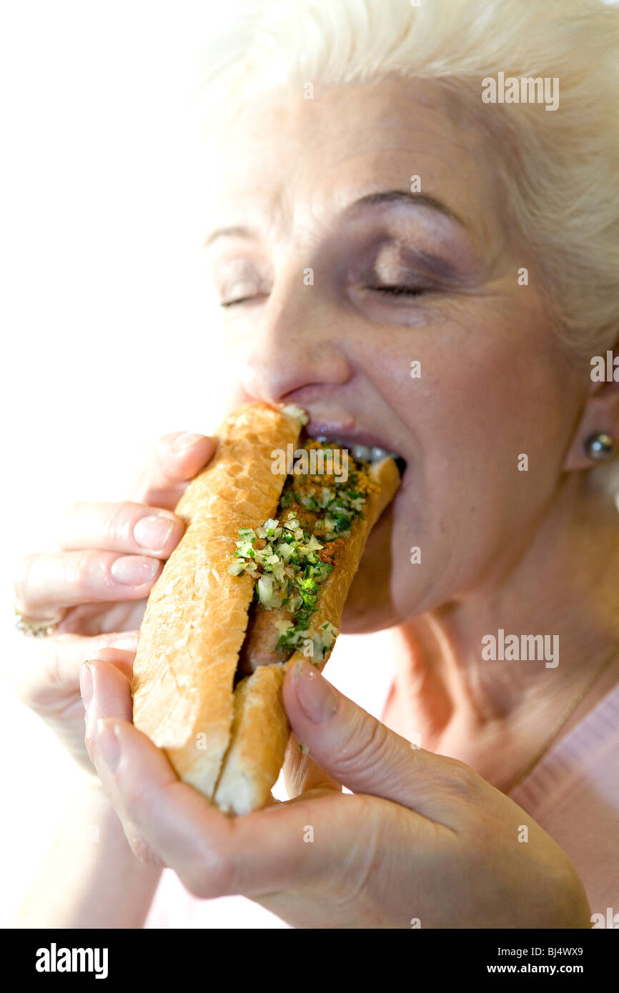 Eine Frau in eine Wurst in einem Baguette zu beißen Stockfoto