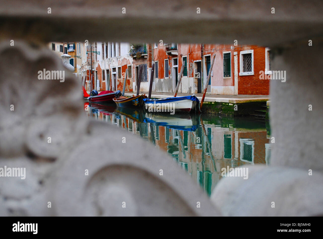 Bunte Häuser und Boote an einem grünen Kanal sind durch ein Loch in eine reich verzierte Wand, Venedig, Italien gesehen. Stockfoto
