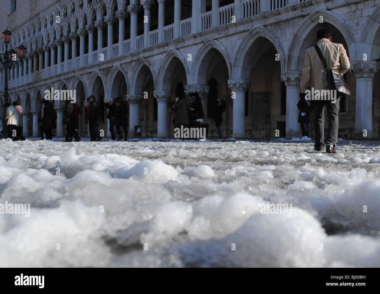 Ein Mann geht über einen Teppichboden des Schnees in den Markusplatz entfernt gegenüber dem Dogenpalast und der Piazzetta Stockfoto