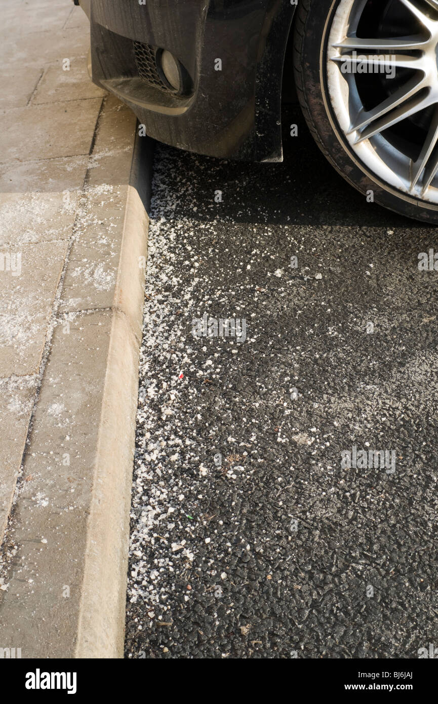 Steinsalz verstreut auf einem Parkplatz neben einem Auto-Rad - schädigt Winterdienst Streusalzverbrauch und Salz, Bremsen und Karosserie gleichermaßen Stockfoto