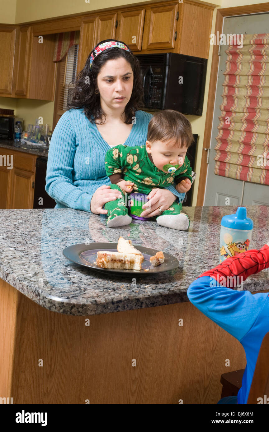 Erschöpfte Hispanic Mutter in ihren Dreißigern versucht, ihre zwei kleinen Kinder zu ernähren im Alter von 4 und 1 Stockfoto