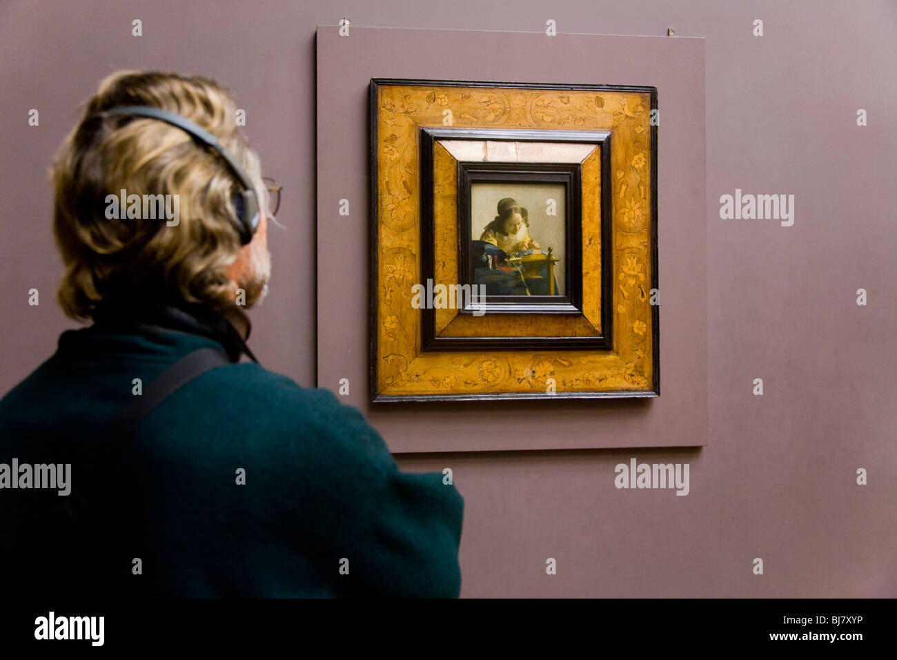 Männliche Touristen tragen Kopfhörer / Kopfhörer Handbuch mit Blick auf die Spitzenklöpplerin Gemälde von Vermeer. Das Louvre, Paris. Frankreich Stockfoto