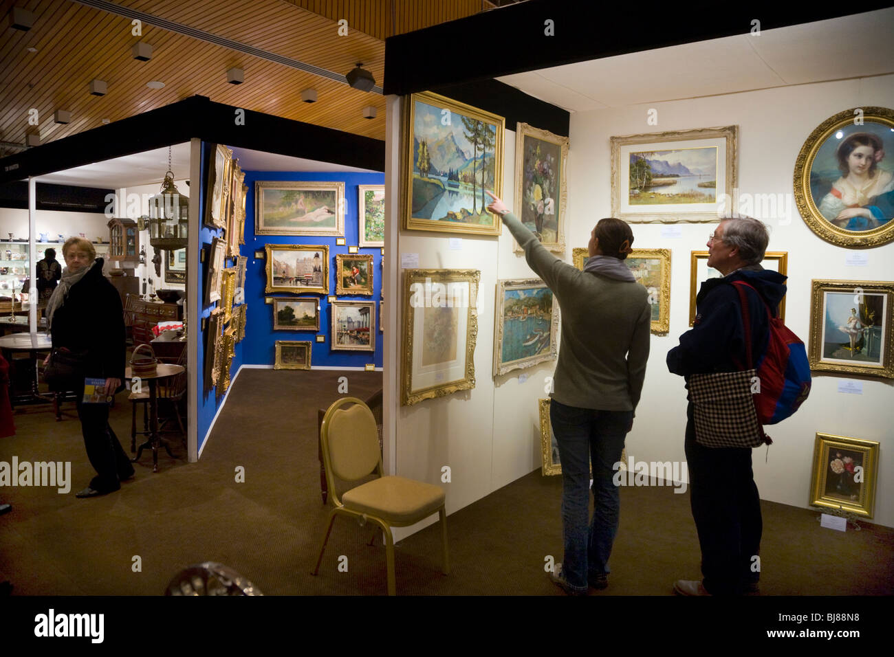 Aussteller / Stall zu verkaufen, antike Gemälde & zwei Kunden auf der & Kunst Antiquitäten Messe, Kensington Town Hall. London. UK Stockfoto