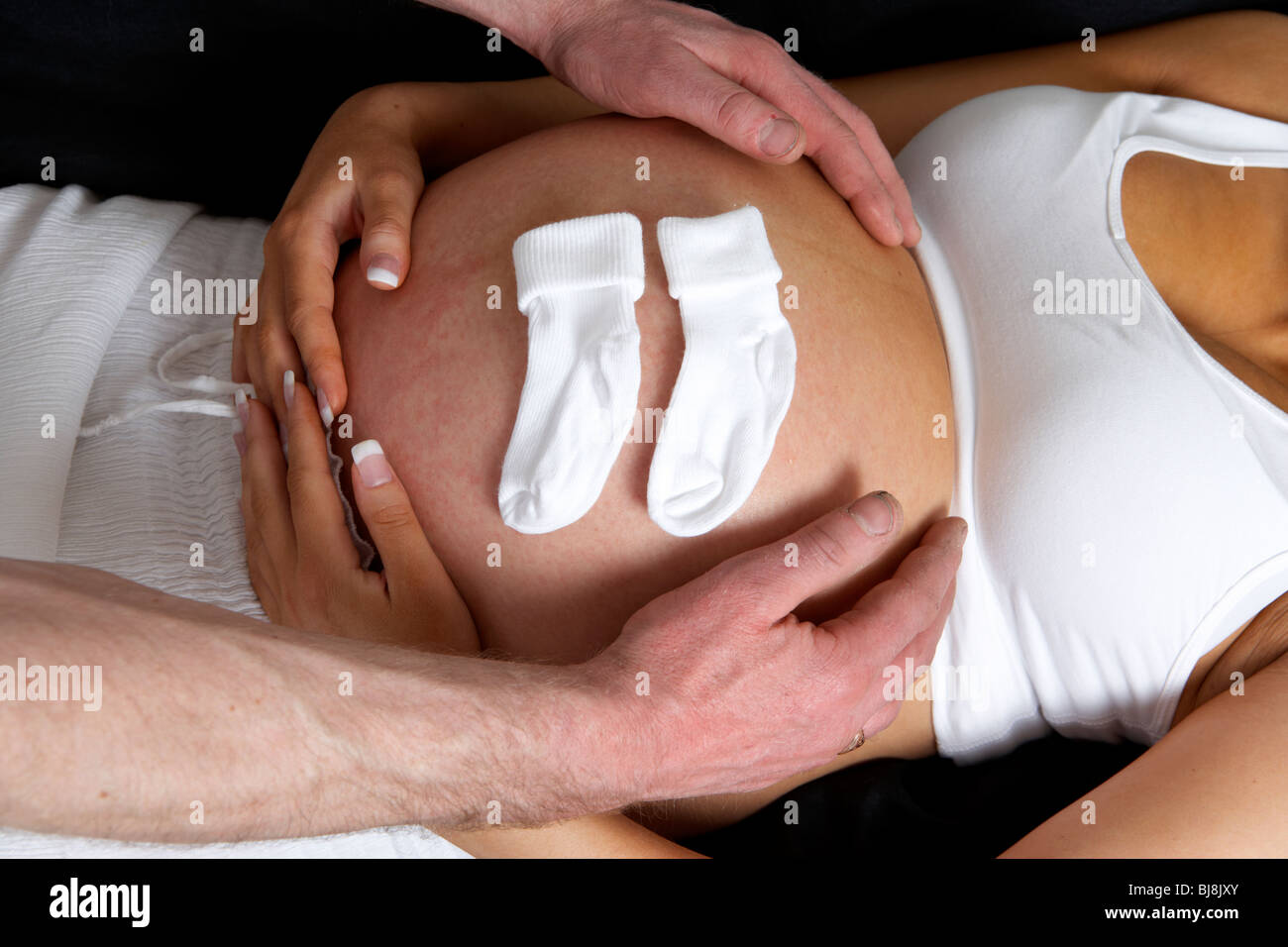8 Monate Hände schwanger 30 Jahre alte Frau mit 37 Jahre alten männlichen Partner auf die Beule mit kleinen Babysocken Stockfoto