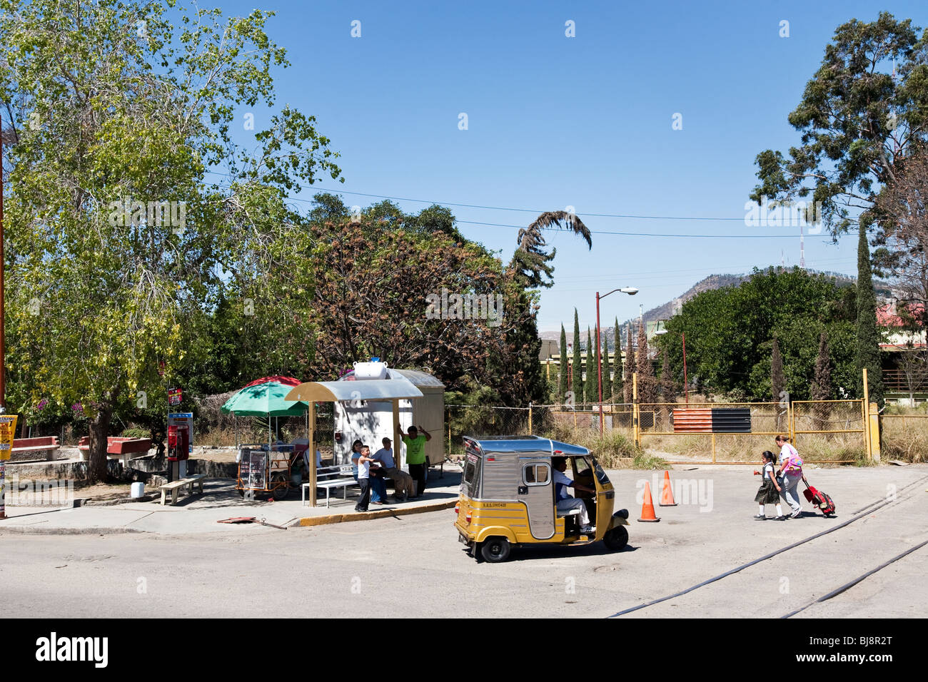 Frau & kleine Schulmädchen Tochter eilen über Kreuzung Bushaltestelle vorbei 3-Rad Mini-Taxi auf Oaxaca Mexico zu ignorieren Stockfoto