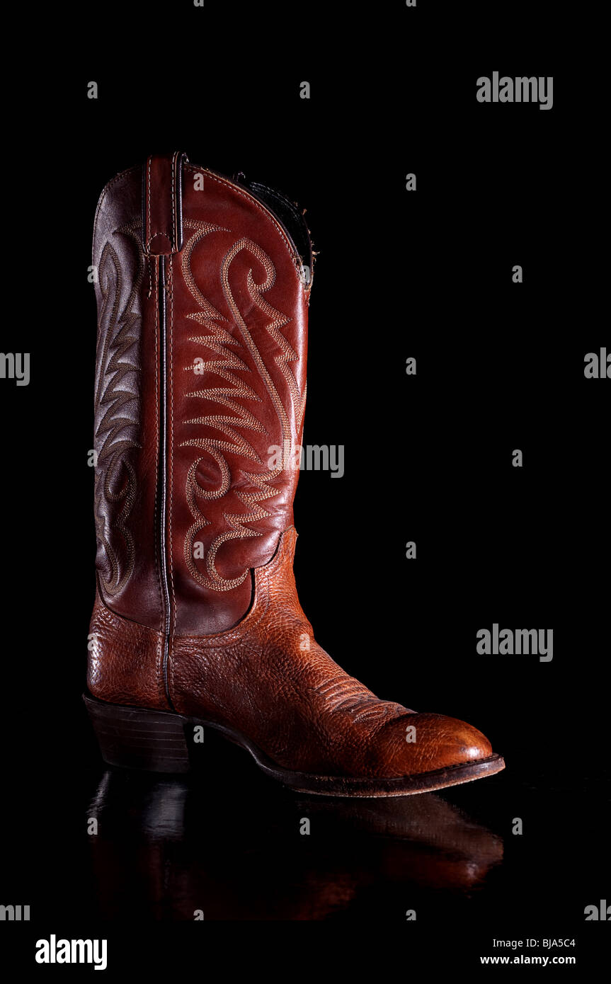 Vertikales Bild ein dunkelbraunes Leder Cowboy Stiefel auf einer reflektierenden Oberfläche Stockfoto