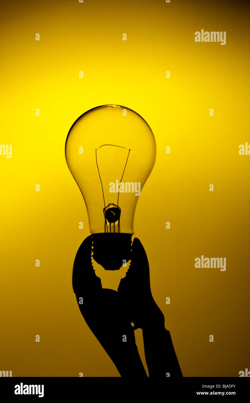 eine Silhouette einer sauberen Glühlampe gehalten in einem Griff auf einen gelben Schein-Hintergrund Stockfoto