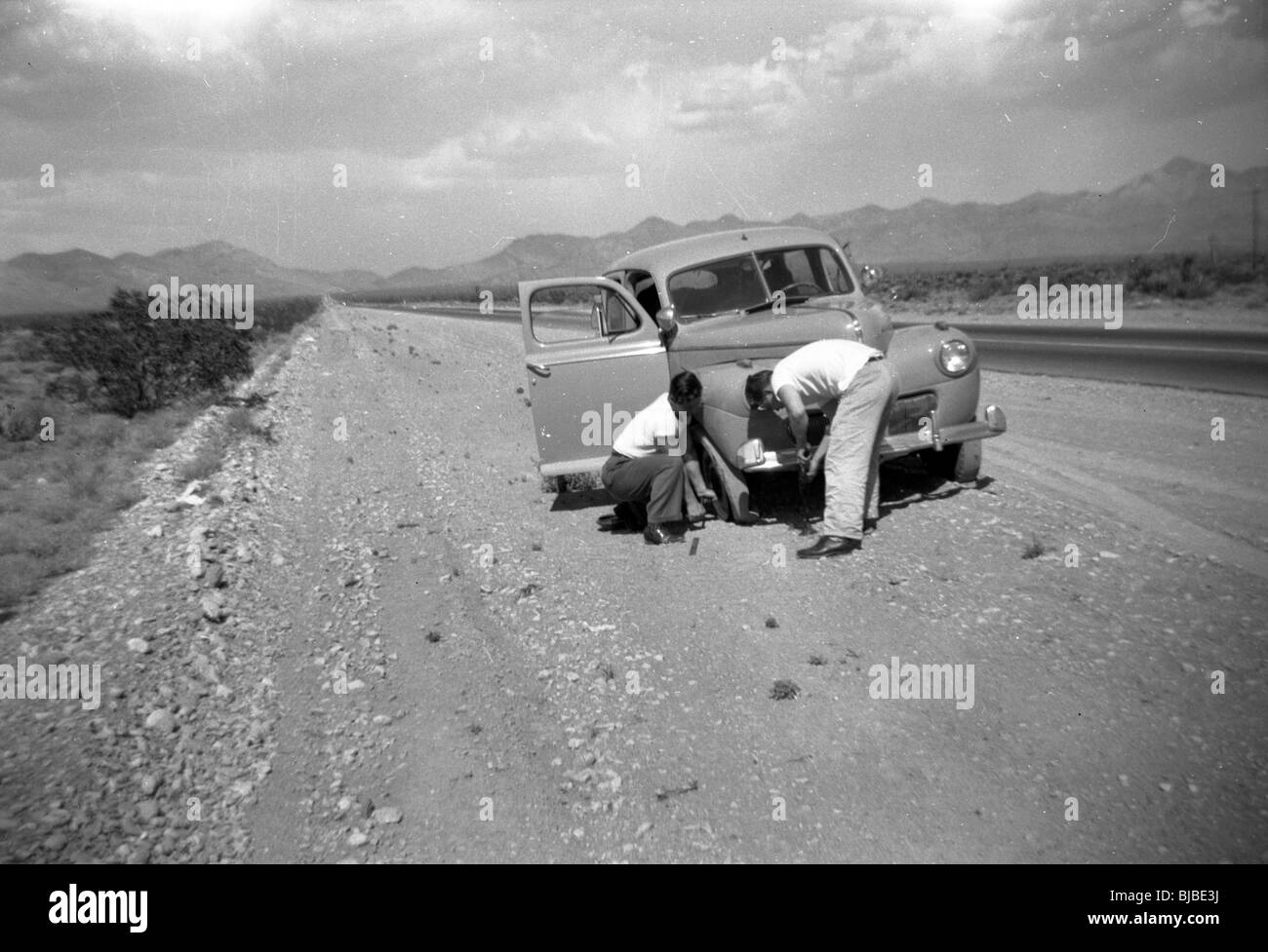 Zwei Reisende ändern eine Reifenpanne in den Südwesten der USA in den 1940er Jahren. Auto reisen Autobahn Berge Wüste desolate leer Stockfoto