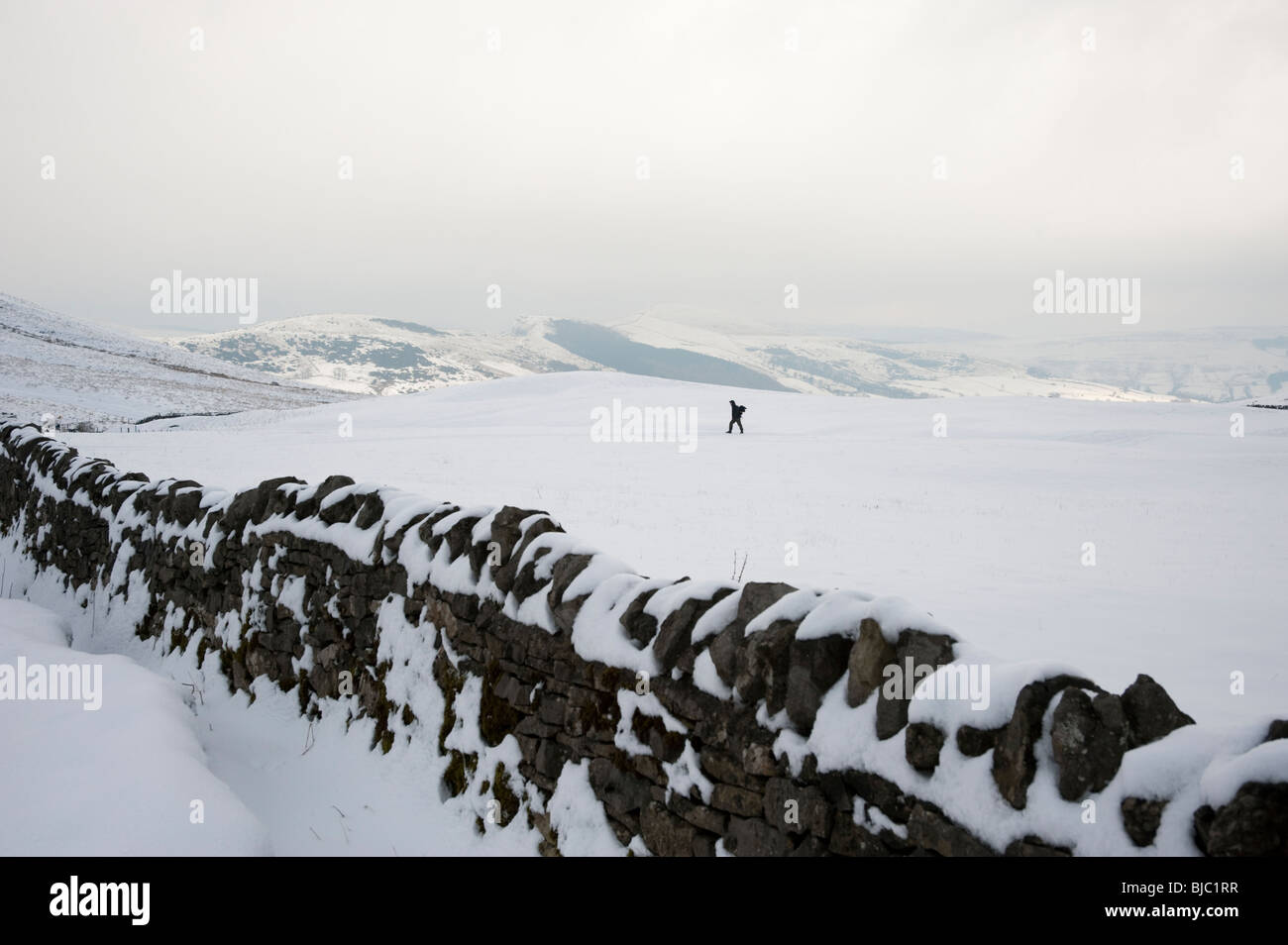 Einsame Figur Wandern im Schnee bedeckt Landschaft, Derbyshire, Peak District, Großbritannien Stockfoto