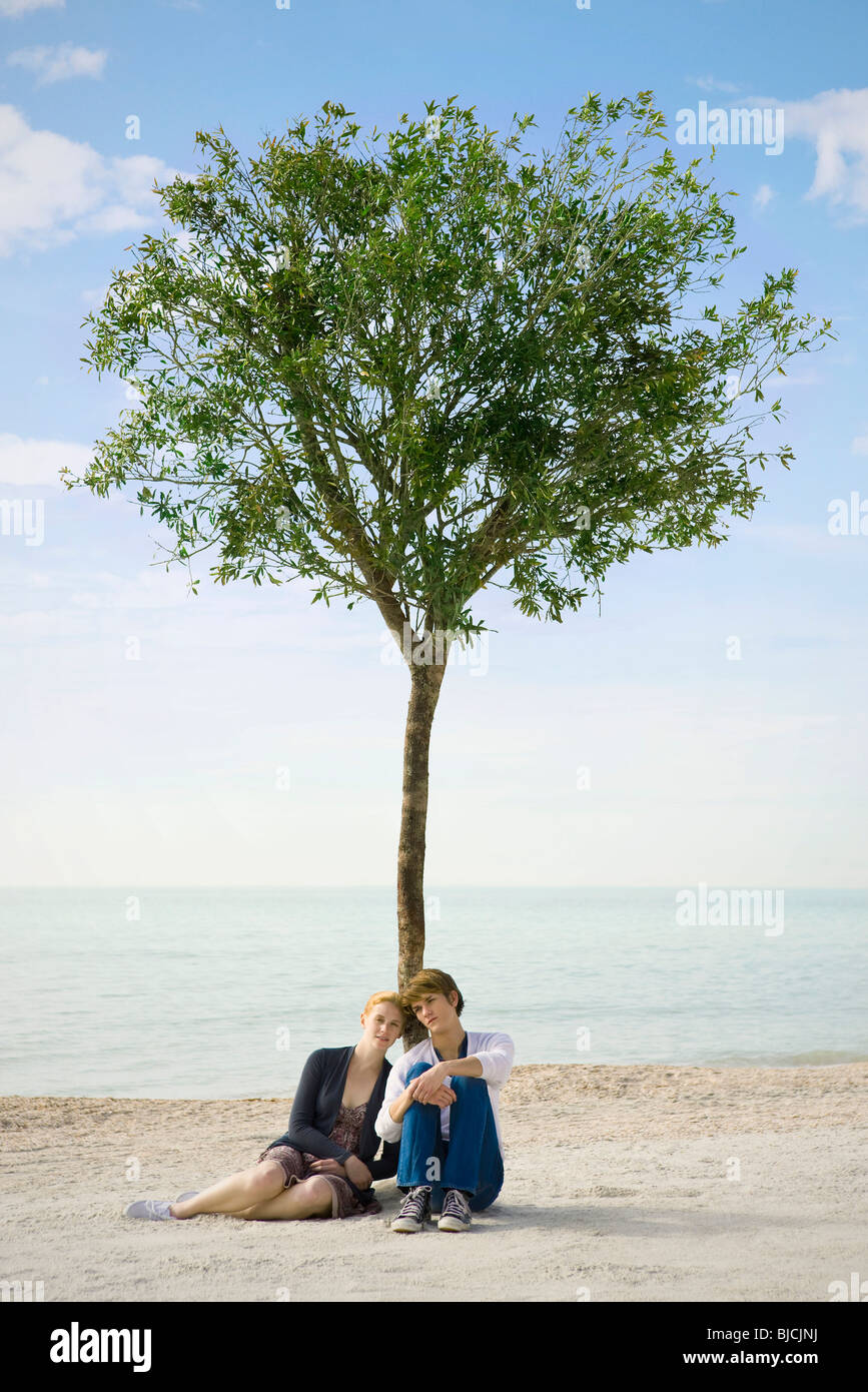 Junges Paar zusammensitzen unter Baum am Strand Stockfoto