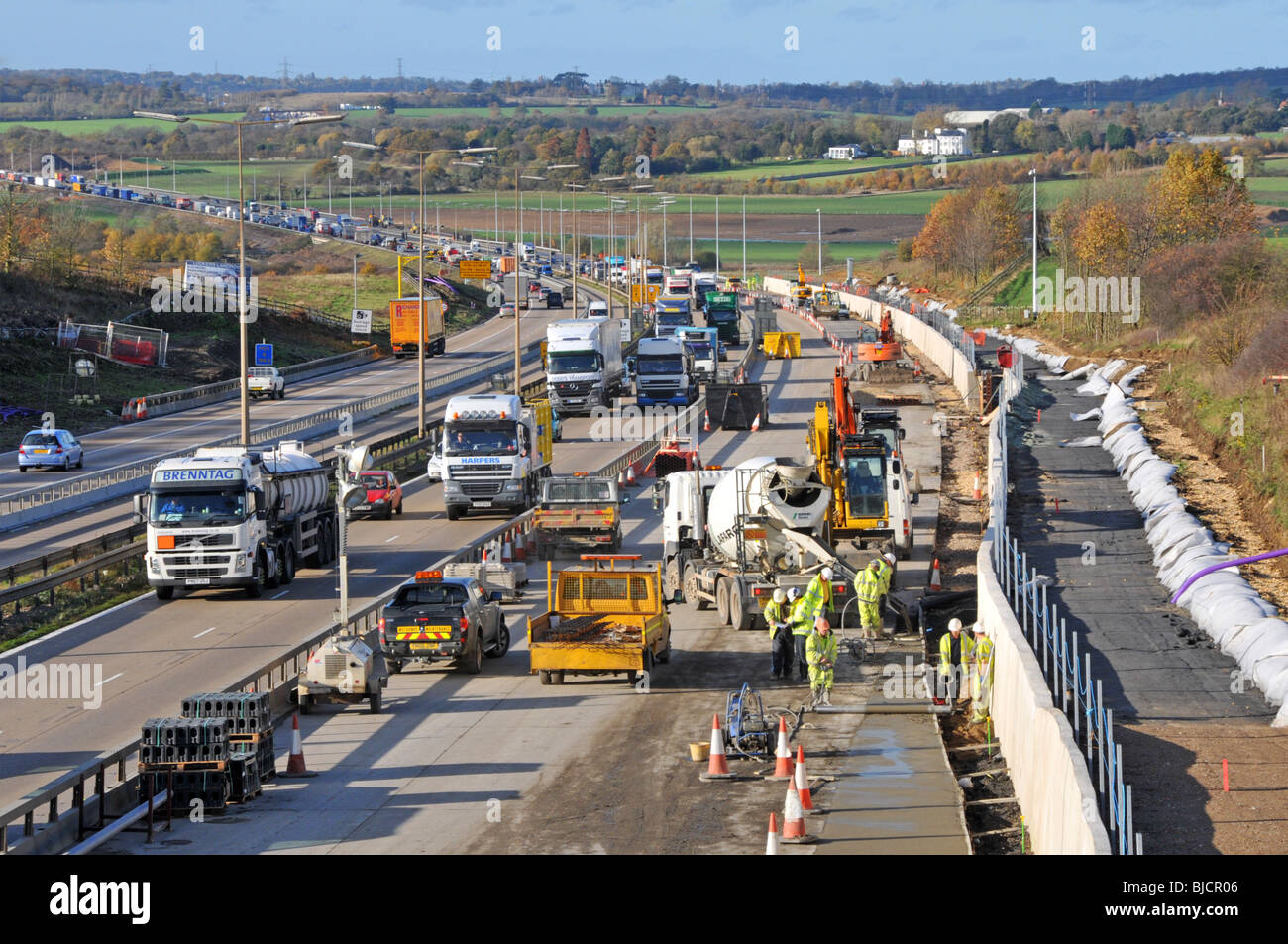 Nahaufnahme des eingeschränkten Verkehrsflusses auf der Fahrspur und Bauarbeiten von Bauarbeitern und Maschinen, die auf der Autobahn M25 beschäftigt sind, die sich auf vier Fahrspuren erweitert, Essex England UK Stockfoto