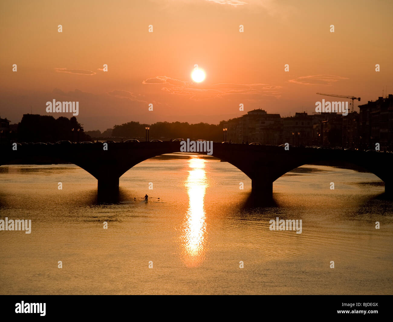 Mann, Rudern auf einem Körper des Wassers mit einer Brücke und Sonnenuntergang im Hintergrund. Stockfoto