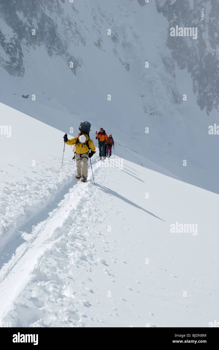 Snowboarder und Skifahrer aufsteigend einen verschneiten Hang im vergletscherten Gelände oberhalb der Vallée Blanche, Chamonix, Frankreich Stockfoto