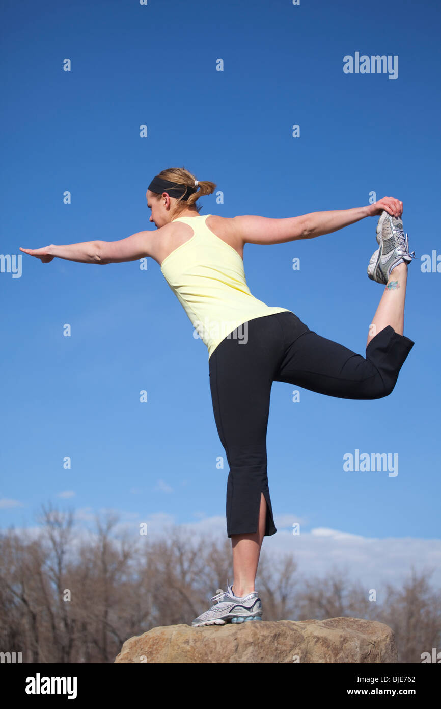 Eine Frau, die Yoga praktiziert und draußen auf einem Felsen steht, mit klarem blauen Himmel Stockfoto
