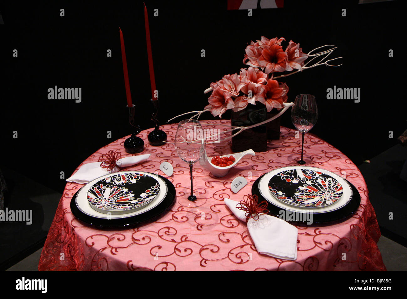 Eleganz Luxus Kerze Besteck Serviette Tafelglas Abendessen rose Vase Dekoration schwarz dunkel rot leuchtende Blume Tisch gedeckt Stockfoto
