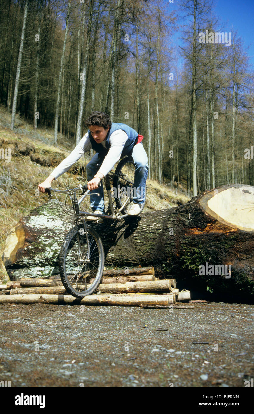 Mann-Mountainbike über einen großen Baum Gliedmaßen und Schnittholz Protokolle Stockfoto