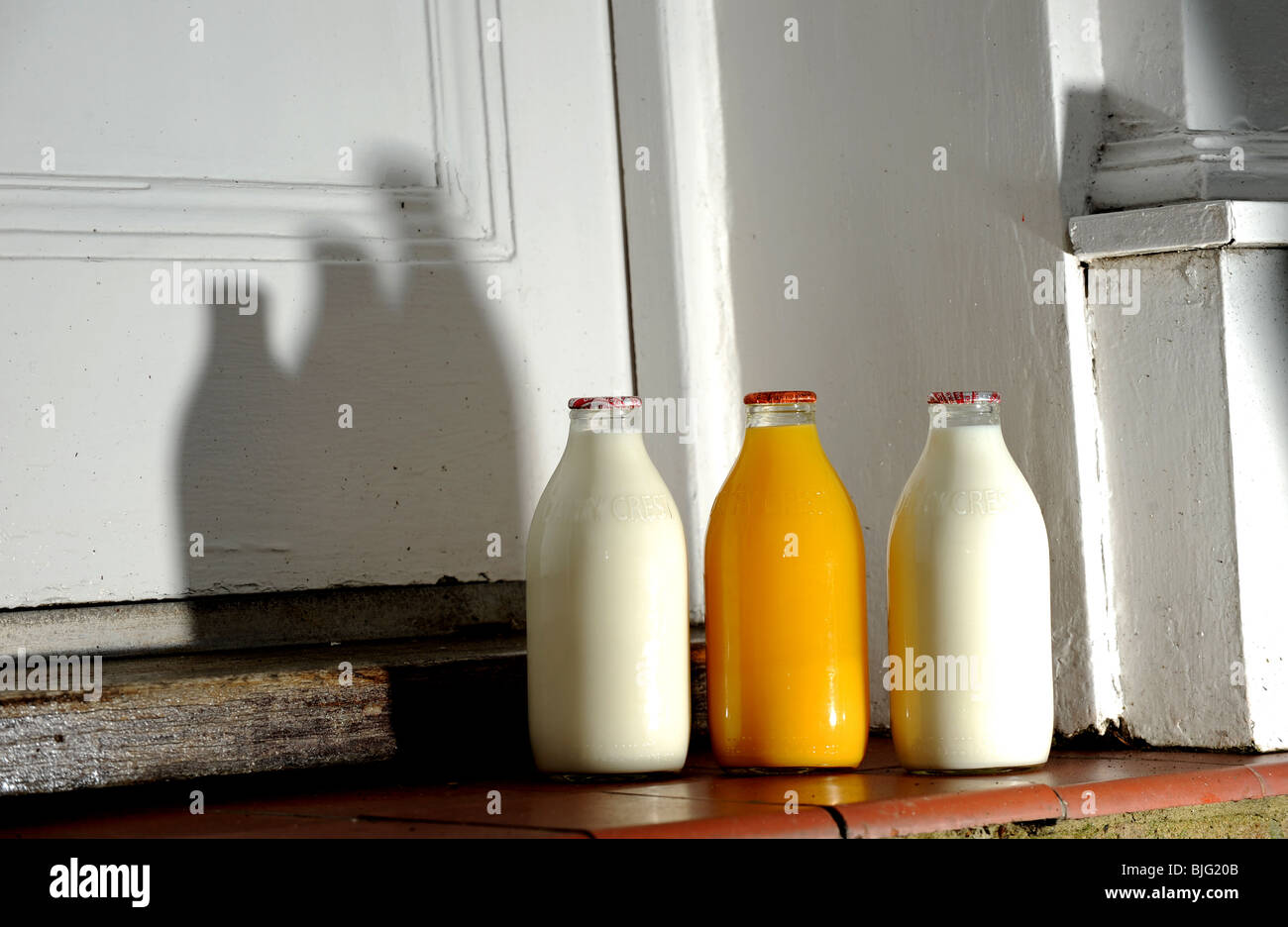 Flaschen Milch und Orangensaft vor einer Haustür geliefert von Milchmann UK Stockfoto