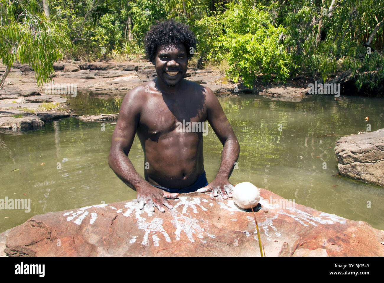 Aborigines junger Mann macht Miko Hand druckt mit weißer Tonerde, er unter Felsen in den Creekbed bei Dukaladjarrang sammelte Stockfoto