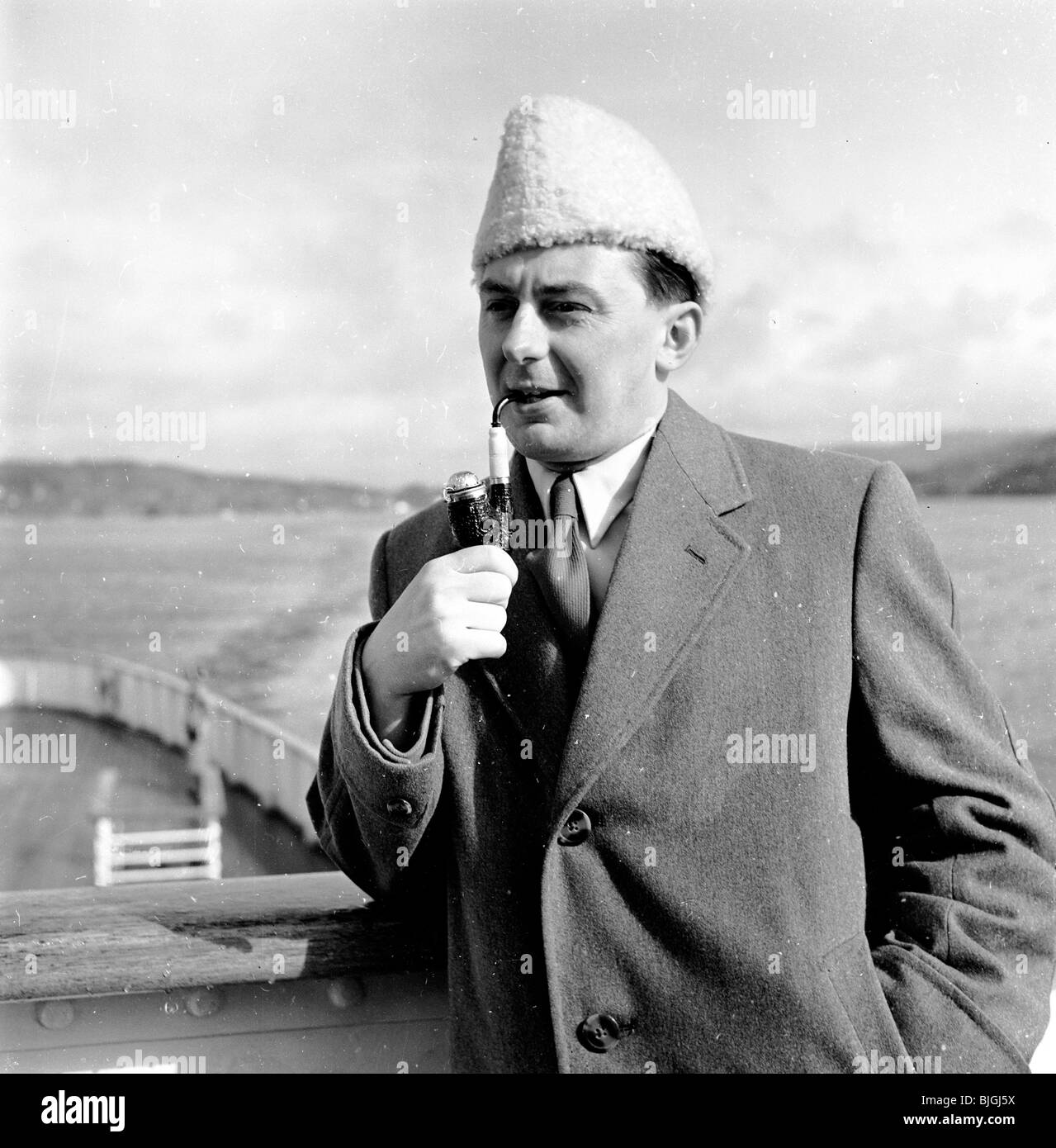 der 1950er Jahre, Bergen, Norwegen. Porträt von gut gekleideten Mann in Mantel und Hut Rauchen einer Pfeife auf oberen Deck eines Kreuzfahrtschiffes steht. Stockfoto