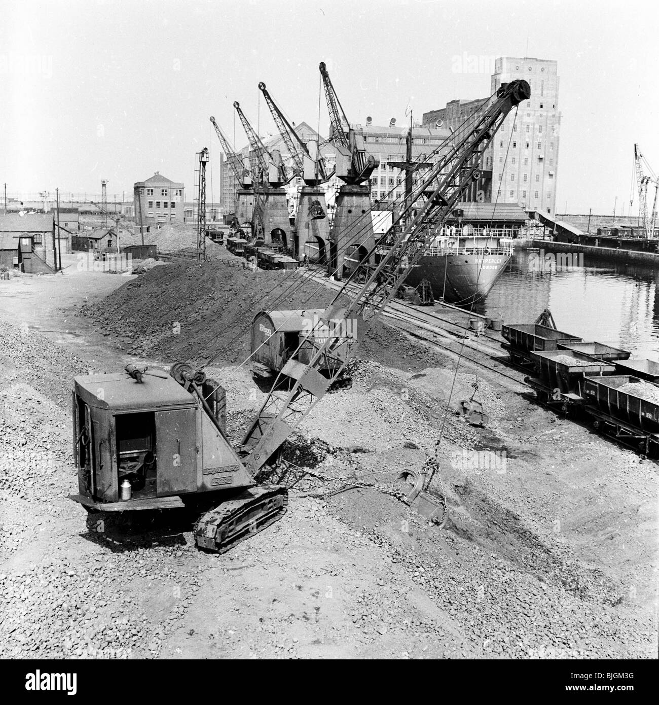 1950s, historische Gesamtansicht einer funktionierenden Werft an den Londoner Docks, wobei Eisenbahnwaggons mit Baumaterial beladen werden. Stockfoto