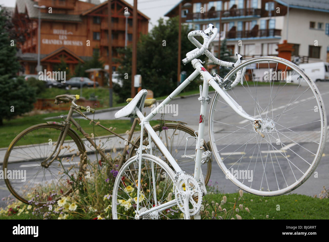 Fahrräder, die wie eine Skulptur am Eingang eines Skiorts in den Alpen, Frankreich, ausgestellt sind, vielleicht um der Tour de France zu gedenken. Eines ist ein stilvolles älteres Fahrrad, während das andere Modell ein weißes, modernes Rennrad ist. Stockfoto