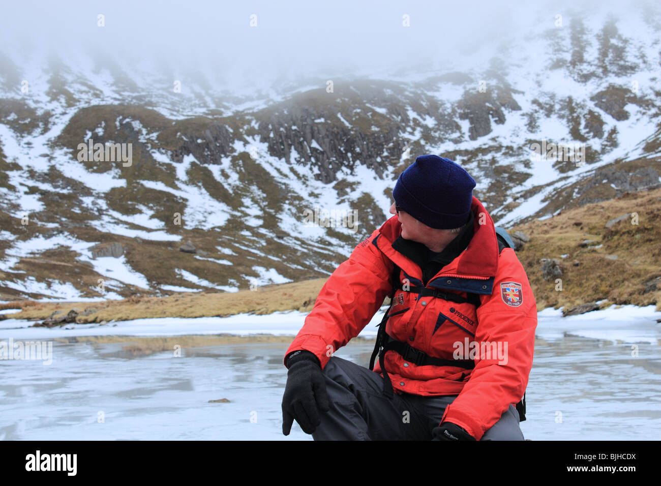 Ein Wanderer ruht von gefrorenen Llyn y Gadair beim Aufstieg Cadair Idris über Fox Weg, Snowdonia-Nationalpark, Gwynedd, Wales, UK Stockfoto