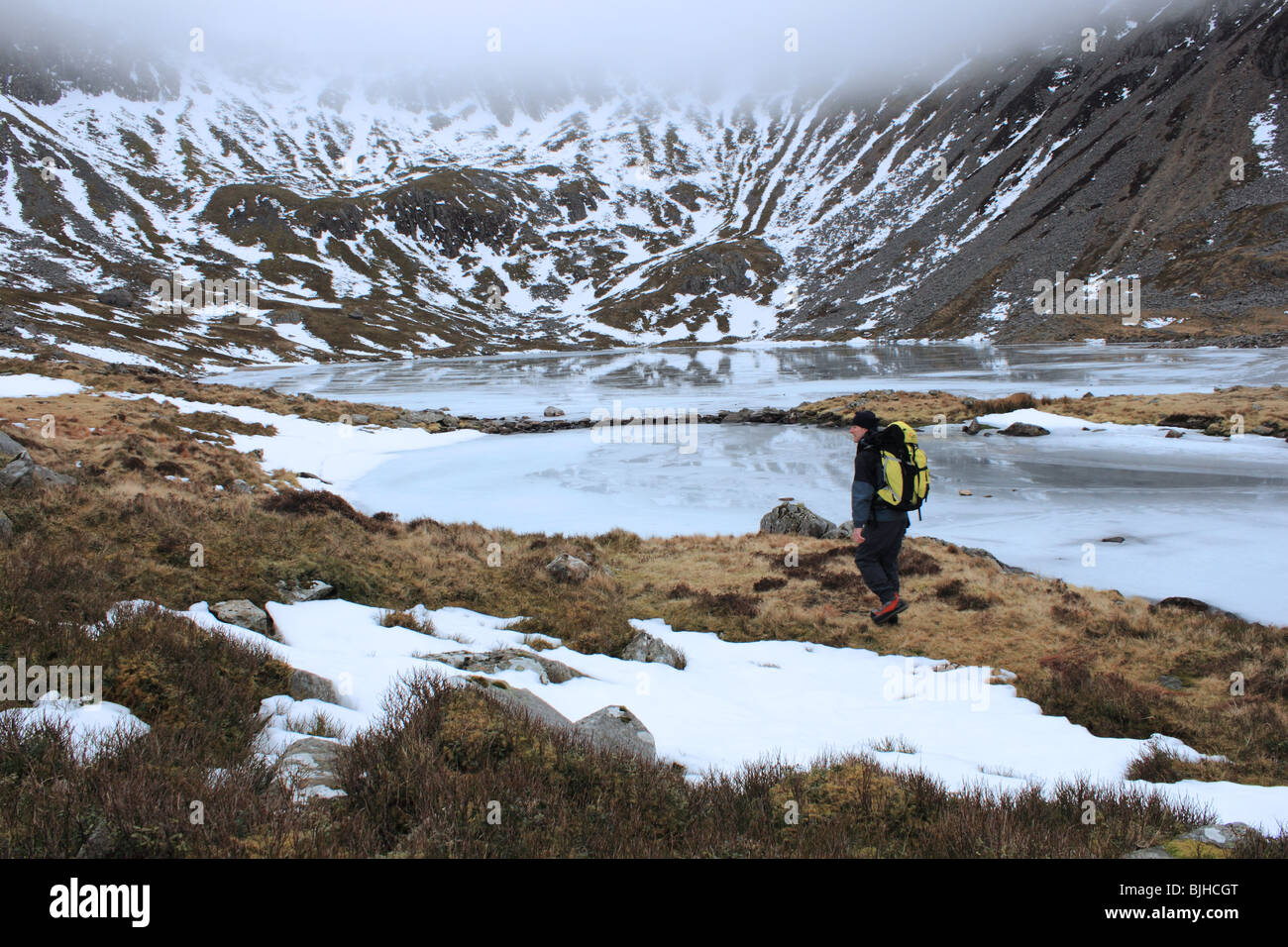 Ein Spaziergänger geht gefrorenes Llyn y Gadair beim Aufstieg Cadair Idris über Fox Weg, Snowdonia-Nationalpark, Gwynedd, Wales, UK Stockfoto