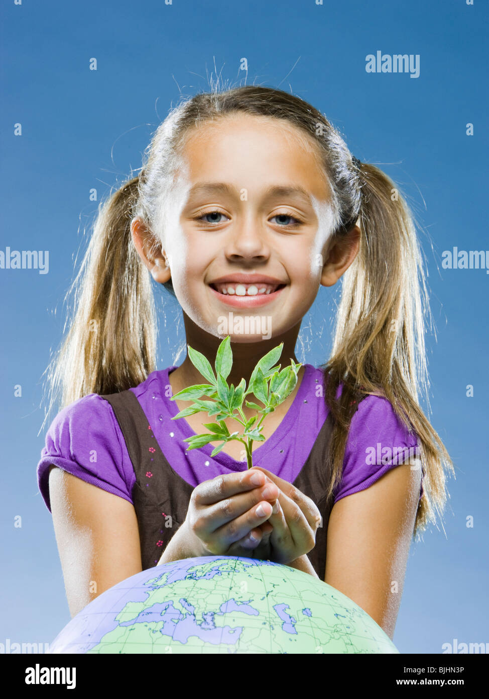 Mädchen schaut in die Kamera hält eine Pflanze vor einem Globus Stockfoto