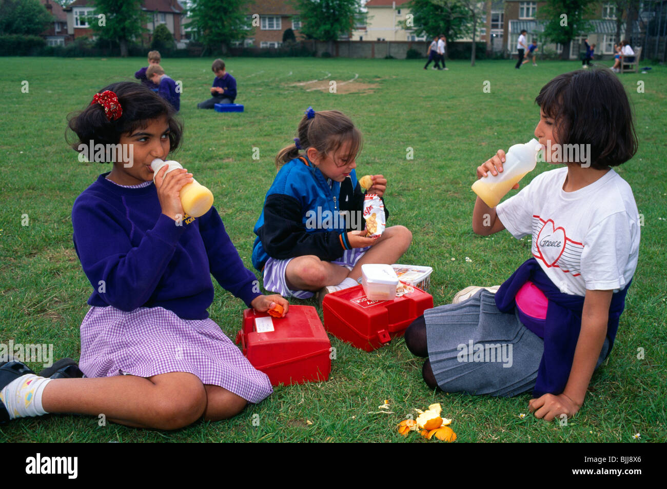 England, East Sussex, Brighton, junge Mädchen, die ihre Lunchpakete draußen auf dem Rasen der Schule Spielfelder. Stockfoto