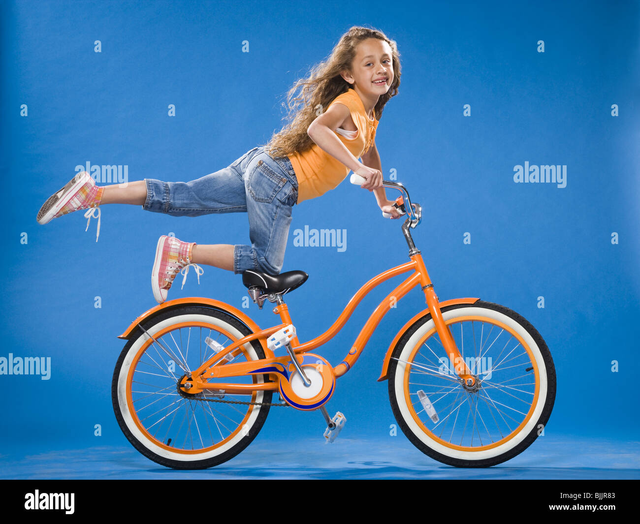 Mädchen auf orange Fahrrad kniend auf Sitz mit Fuß Stockfoto
