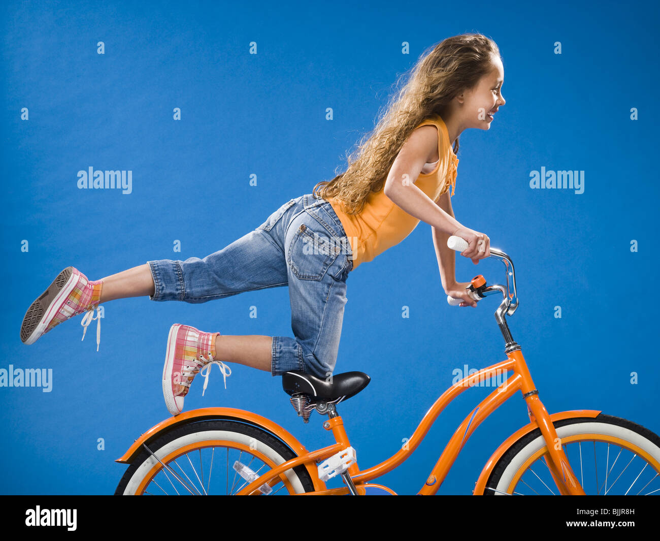 Mädchen auf orange Fahrrad kniend auf Sitz mit Fuß Stockfoto