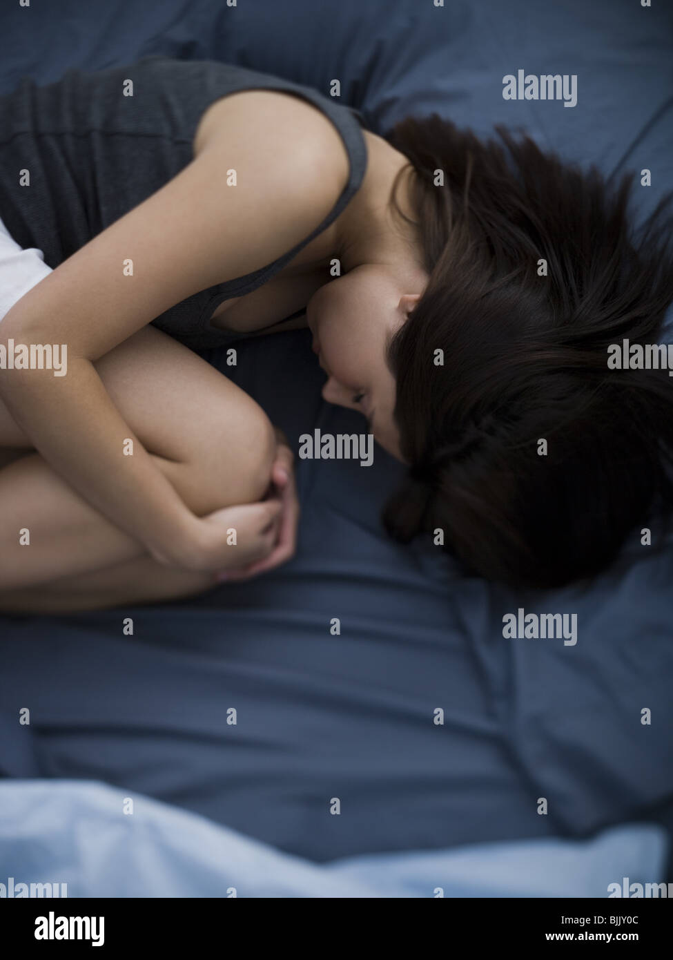 Frau im Bett schläft zusammengerollt Stockfoto