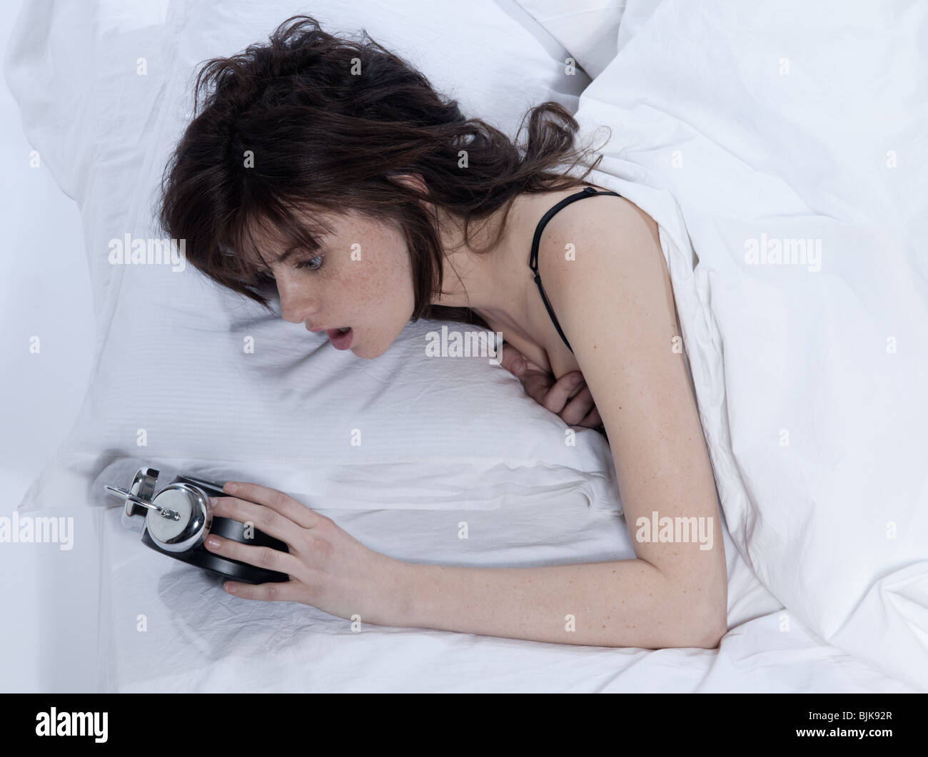 junge Frau in einem weißen Blatt Bett auf weißem Hintergrund Stockfoto