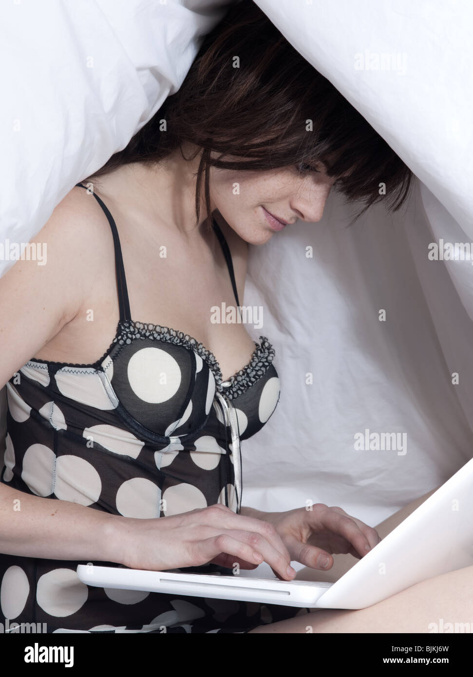 junge Frau in einem weißen Blatt Bett auf weißem Hintergrund mit einem pc Computer laptop Stockfoto