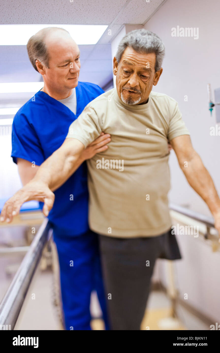 Physiotherapeuten unterstützen einen älteren Mann mit einem Bein in unmittelbarer Stockfoto