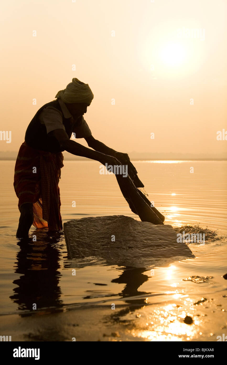 Ein indischer Mann, ein Dhobi wäscht Kleidung in den Fluß Ganga (Ganges) in Varanasi, Indien Stockfoto