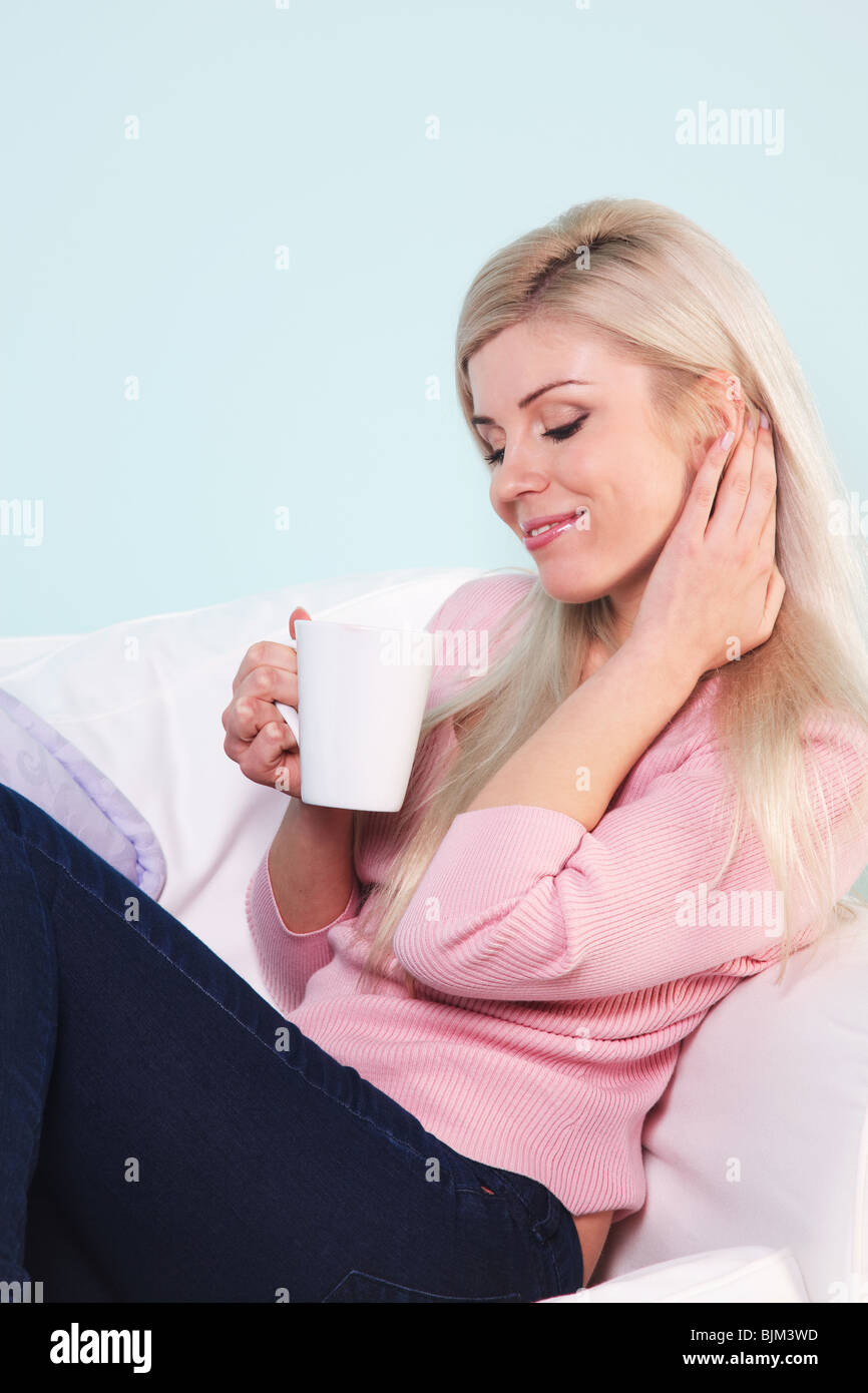 Blonde Frau saß in einem Sessel mit einer Tasse Tee. Stockfoto