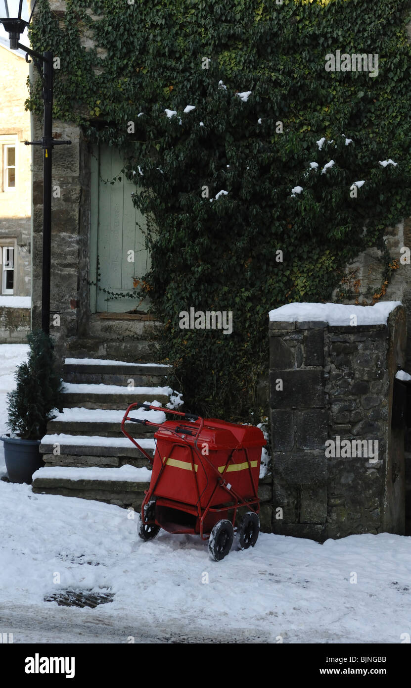 Ein Royal Mail Delivery Cart drausen ein Efeu bedeckt Häuschen auf einer schneebedeckten Straße. Stockfoto