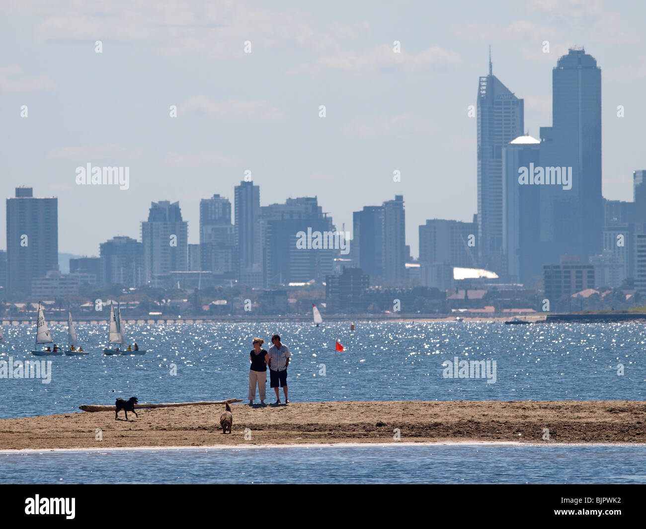 KÜSTEN BLICK AUF PORT PHILLIP BAY MIT PAAR UND HUNDE AUF SAND SPIT UND SKYLINE VON MELBOURNE AM HORIZONT VICTORIA AUSTRALIEN Stockfoto