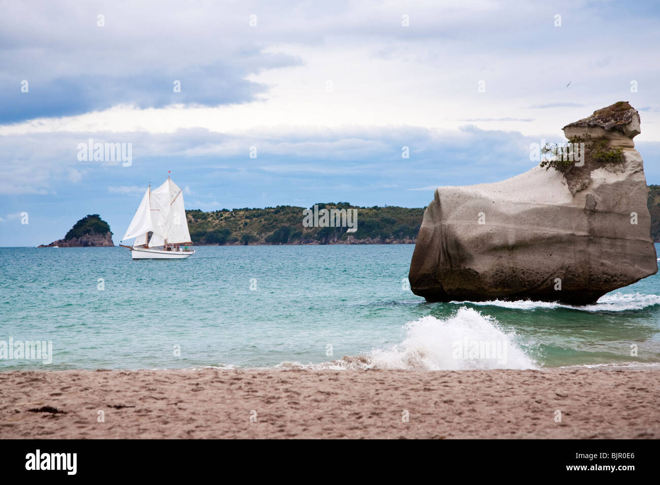 Felsformationen am Wasserrand, mit Segelboot im Hintergrund, Coromandel Peninsula, Neuseeland Stockfoto