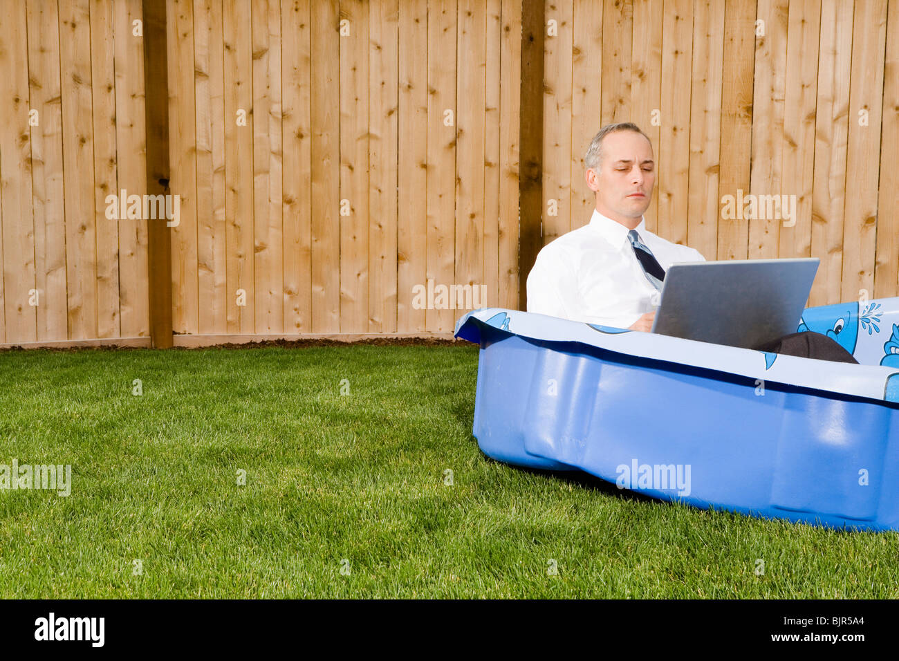 Geschäftsmann in einem Hinterhof-Pool auf einem laptop Stockfoto