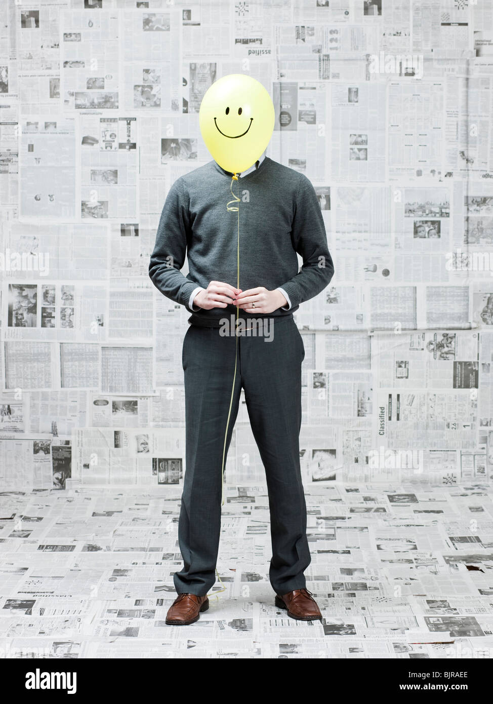 Junger Mann für Gesicht mit Smiley Ballon in Zeitung Zimmer Stockfoto
